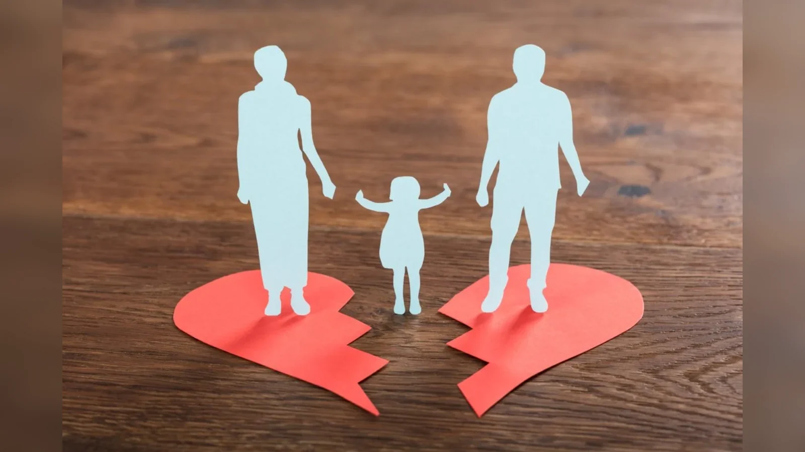 Paper cutouts of two adults and a child on separated halves of a red broken heart, symbolizing family separation after divorce